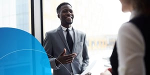 Man in suit smiling and gesturing to person in front of him 