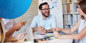 man sitting at desk smiling at a female coworker 