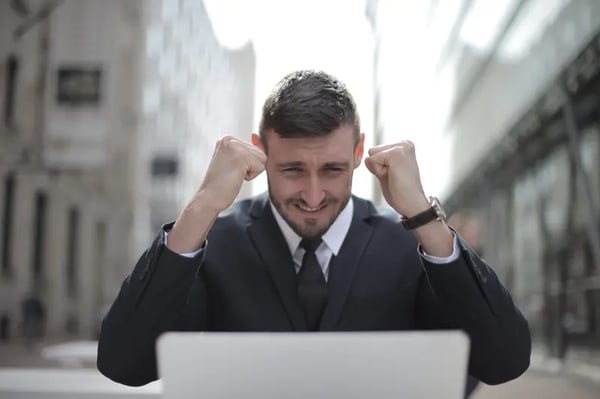 Man looking into laptop with fists in the air showing excitement