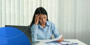 Woman sitting at desk with laptop next to her looking stressed 